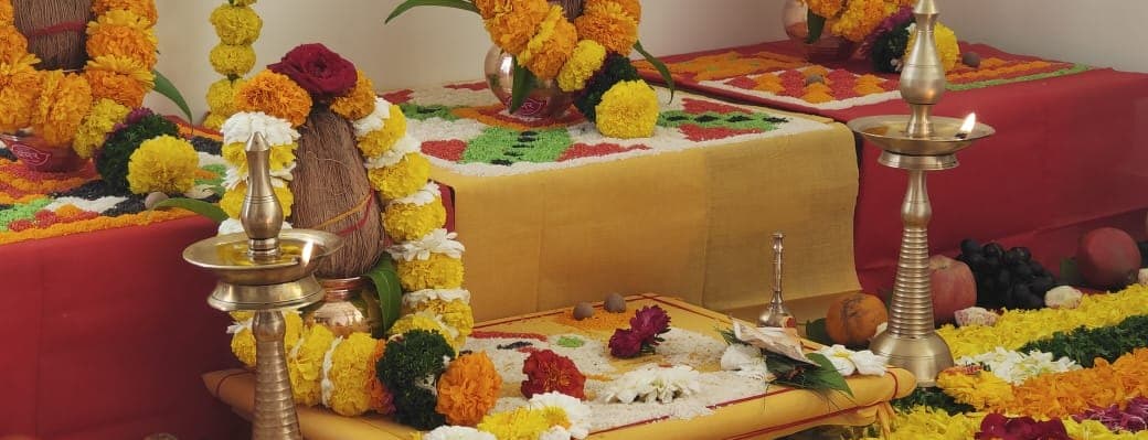 Brass lamps beside a garlanded kalash on an altar dressed with marigolds