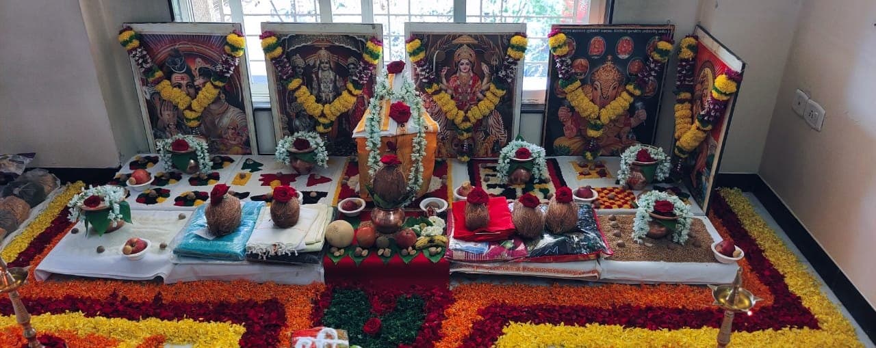 Puja altar with garlanded deity portraits, kalash and a floral rangoli